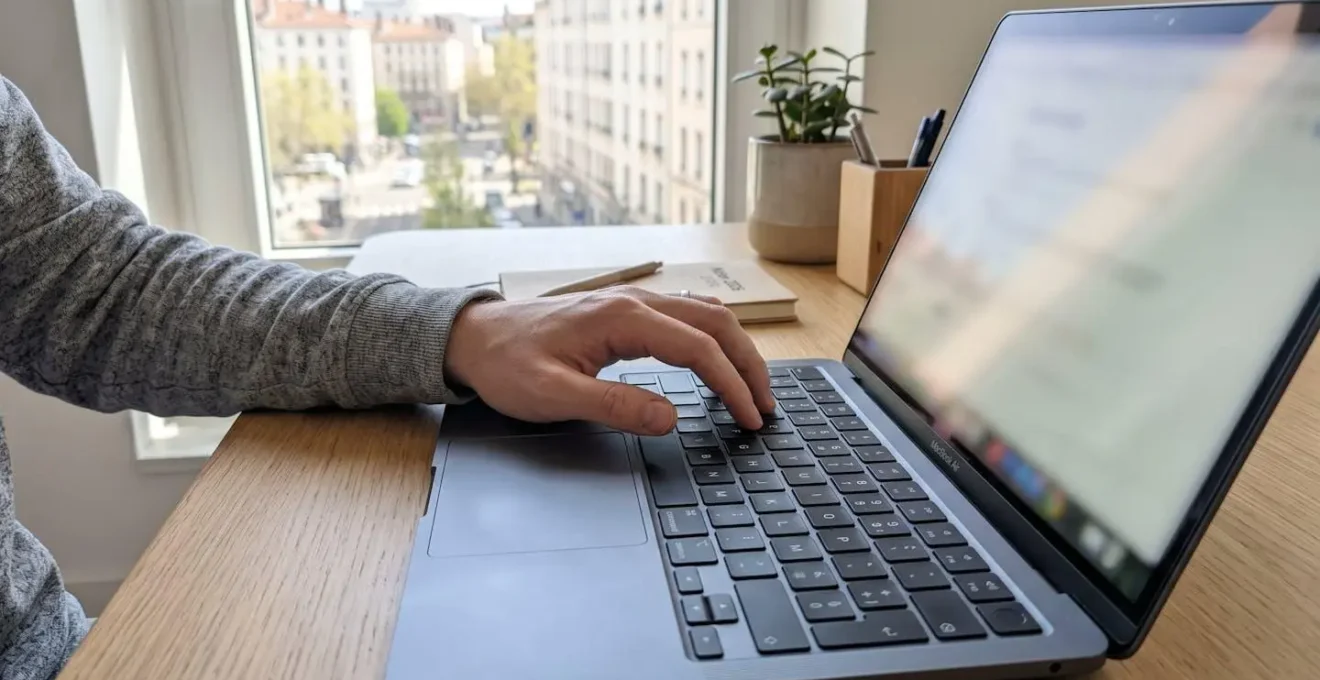Gros plan sur une main tapant sur le clavier d'un ordinateur portable moderne, écran totalement flouté en arrière-plan, dans un bureau épuré